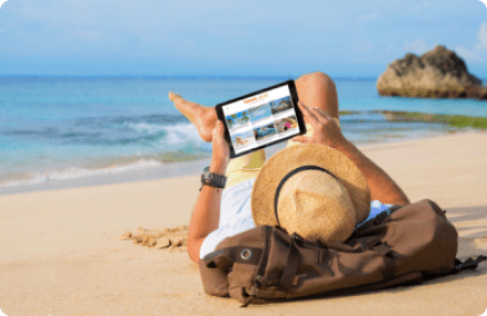 a man with a hat and backpack laying on the beach using a tablet