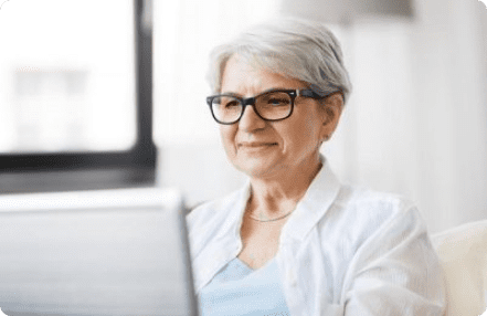 an older woman with glasses sitting on a couch with a laptop
